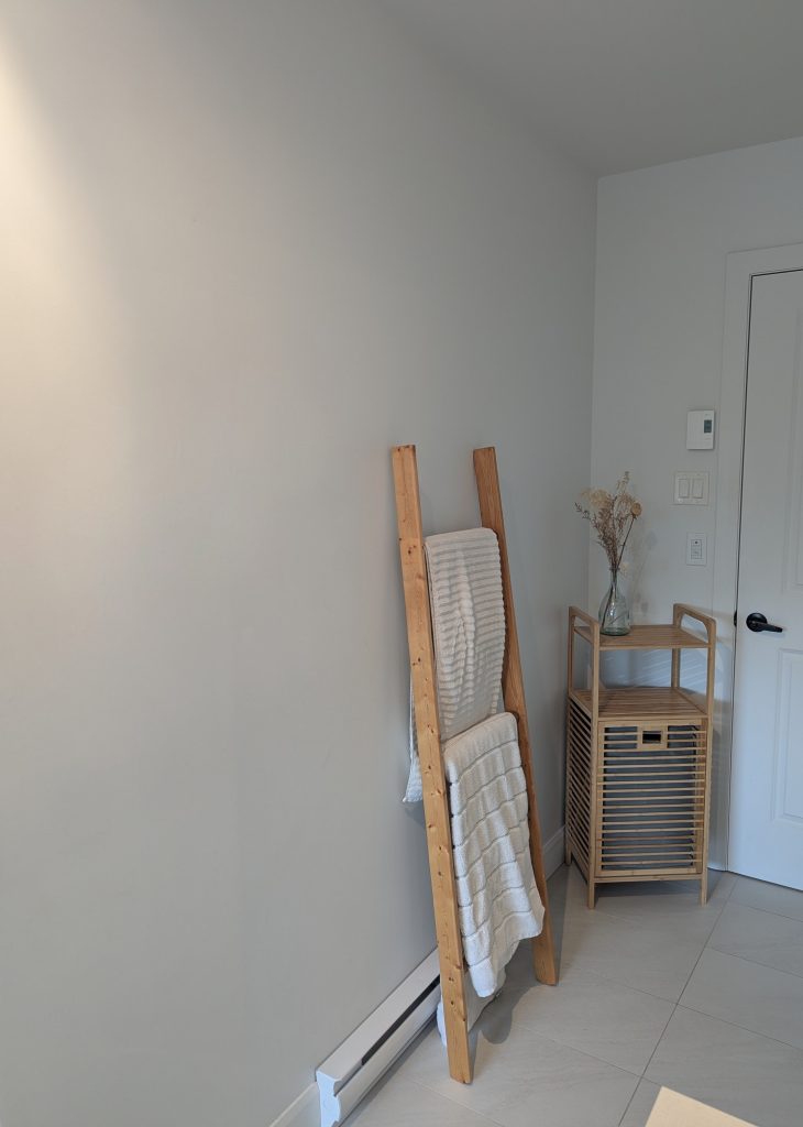 Mur blanc uni dans une salle de bain de style zen avec une échelle en bois pour serviettes et un petit meuble de rangement en bambou.